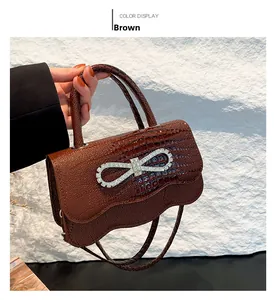 Detail of brown crocodile pattern handbag with rhinestone bow and wavy bottom edge