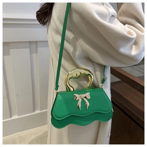 Detail of green crossbody bag featuring a wavy flap and golden bow ornament on model