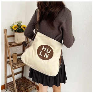 Detail of a large cream canvas tote bag featuring brown leather straps and round logo patch