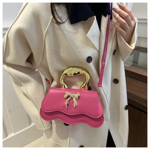 Detail of rose pink handbag featuring a wavy base and golden heart butterfly buckle