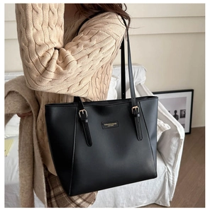 Detail of black textured leather tote bag with gold buckles worn over a beige sweater