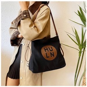 Detail of a large canvas shoulder bag featuring brown leather straps and a logo patch