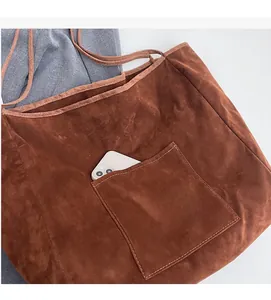 Detail of brown suede tote bag featuring a functional front pocket holding a phone
