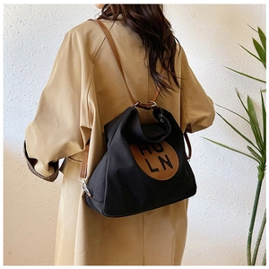 Detail showing versatile black canvas bag with brown leather straps and logo patch
