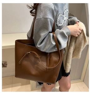 Detail showing high-capacity brown leather tote bag with long straps worn by model