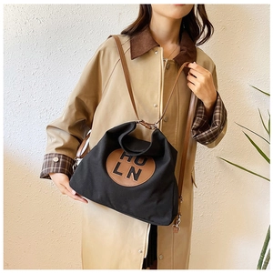 Detail of minimalist canvas tote bag with brown leather patch and long shoulder strap