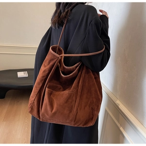 Detail of a large brown suede tote bag featuring a front pocket and long shoulder straps