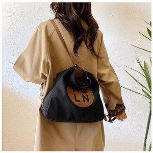 Detail of black canvas Hobo bag with brown leather logo patch and slim shoulder strap