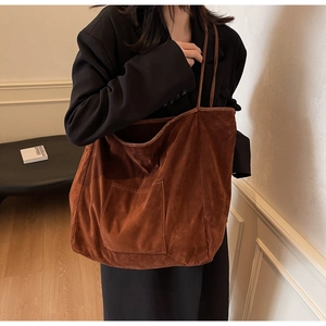 Detail of a large brown suede tote bag with front pocket shown in elegant indoor setting