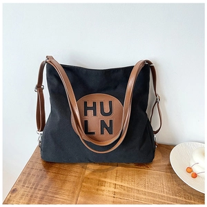 Detail of black canvas tote bag with brown leather handles and circular logo patch on a table