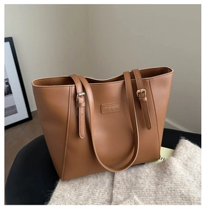 Detail of a brown leather tote bag showing textured finish and adjustable gold buckle straps
