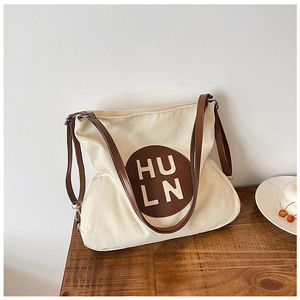 Detail of canvas tote bag showing brown leather patch with HULN logo and premium stitching