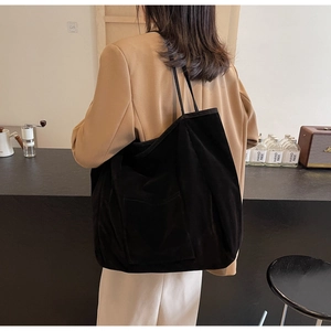 Detailed view of a black corduroy tote bag with a functional front pocket on a model
