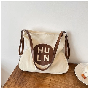 Close-up of cream canvas tote bag with brown leather HULN logo patch on wooden table