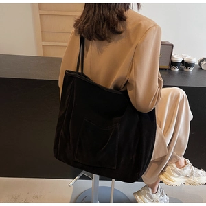 Detail of black corduroy tote bag with large external pocket shown in a lifestyle setting