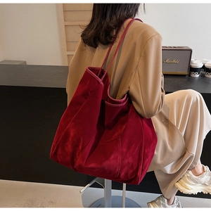 Detail of a large burgundy velvet tote bag worn on shoulder showing its soft texture