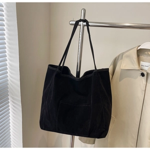 Detail of a large black suede tote bag with front pocket hanging on a metal hanger