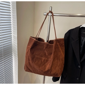 Detail of caramel brown suede tote bag featuring a functional front pocket and slim strap