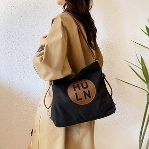 Large black canvas tote bag with brown leather handles and logo patch for daily commute