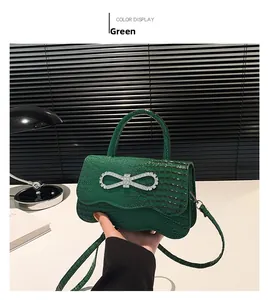 Detail of green handbag with crocodile texture and sparkling rhinestone bow buckle