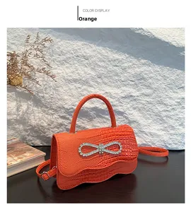 Close-up of orange crocodile pattern handbag featuring a sparkling rhinestone bow buckle
