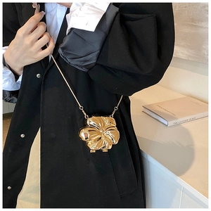 Detailed view of 3D metallic flower-shaped chain bag in gold finish on black blazer