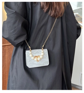 Detail of grey marble mini crossbody bag with pearl handle and golden heart clasp on black coat