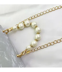 Detail of a pearl handbag strap with gold chains, rhinestone beads, and lobster clasps
