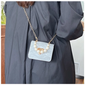 Detailed shot of a mini crossbody bag featuring pearl handle and golden heart buckle