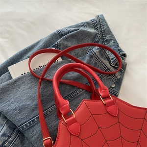 Detail of red spider web crossbody bag with gold hardware on denim background