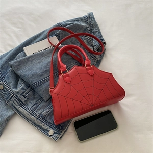 Detail of red spider web bag with dual handles on a bed with lifestyle props