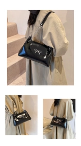 Detail of black patent leather tote bag with silver bow buckle and chain strap shown on model