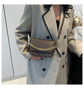 Detail of brown monogram crossbody bag with gold chain and branded woven strap on a blazer