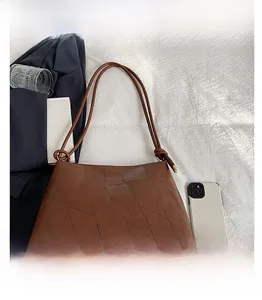 Flat lay of brown patchwork tote bag with accessories on white fabric background