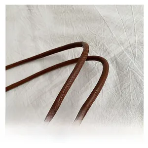 Detail shot of the textured brown leather handle and fine stitching on a tote bag