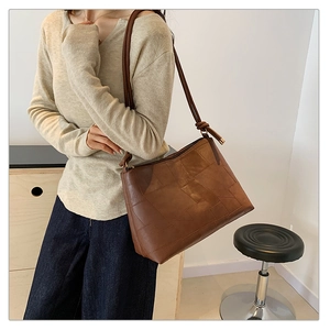Detail of a brown patchwork tote bag featuring geometric faux leather and gold hardware