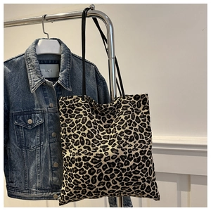 Detail of leopard print tote bag with slim cord handles hung on a denim jacket