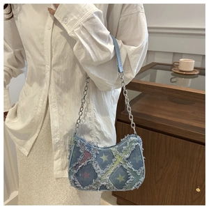 Detail of blue denim crescent bag featuring star patterns and distressed raw edges