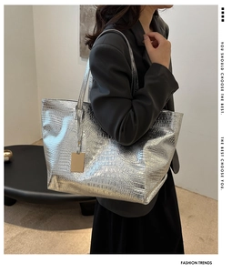 Detail of silver crocodile-embossed tote bag with metallic sheen and gold metal tag