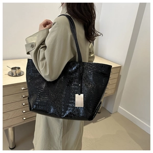 Close-up of a black crocodile pattern tote bag shown with a khaki trench coat