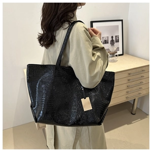 Detail of a large black tote bag with crocodile texture worn by a model in a warm room
