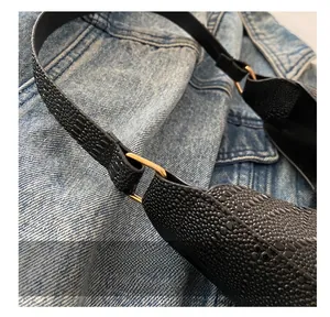 Dettaglio della texture in pelle nera e fibbia ad anello in metallo dorato della borsa