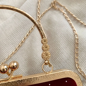 Detail of red velvet evening bag with gold floral handle and carved metal frame