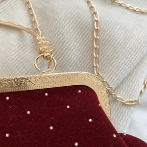 Detail of red velvet evening bag with gold floral engraving and metal chain strap