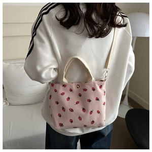 Detail view of pink corduroy shoulder bag featuring all-over red strawberry patterns