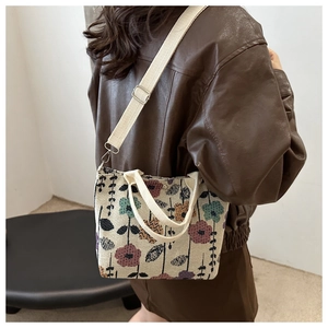 Detail view of a floral jacquard crossbody bag with off-white woven straps on a model