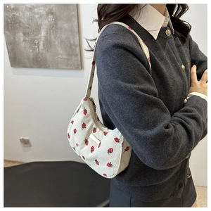 Detail view of white corduroy crescent bag with strawberry pattern on model shoulder