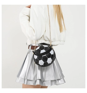 Detail of soccer-shaped crossbody bag with gold chain strap on a stylish white outfit