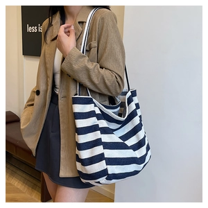 Detail of a large canvas tote bag with navy stripes shown on model in a blazer