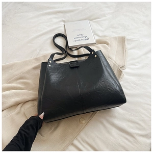 Close-up of black pleated faux leather tote bag with silver rivets and fashion text